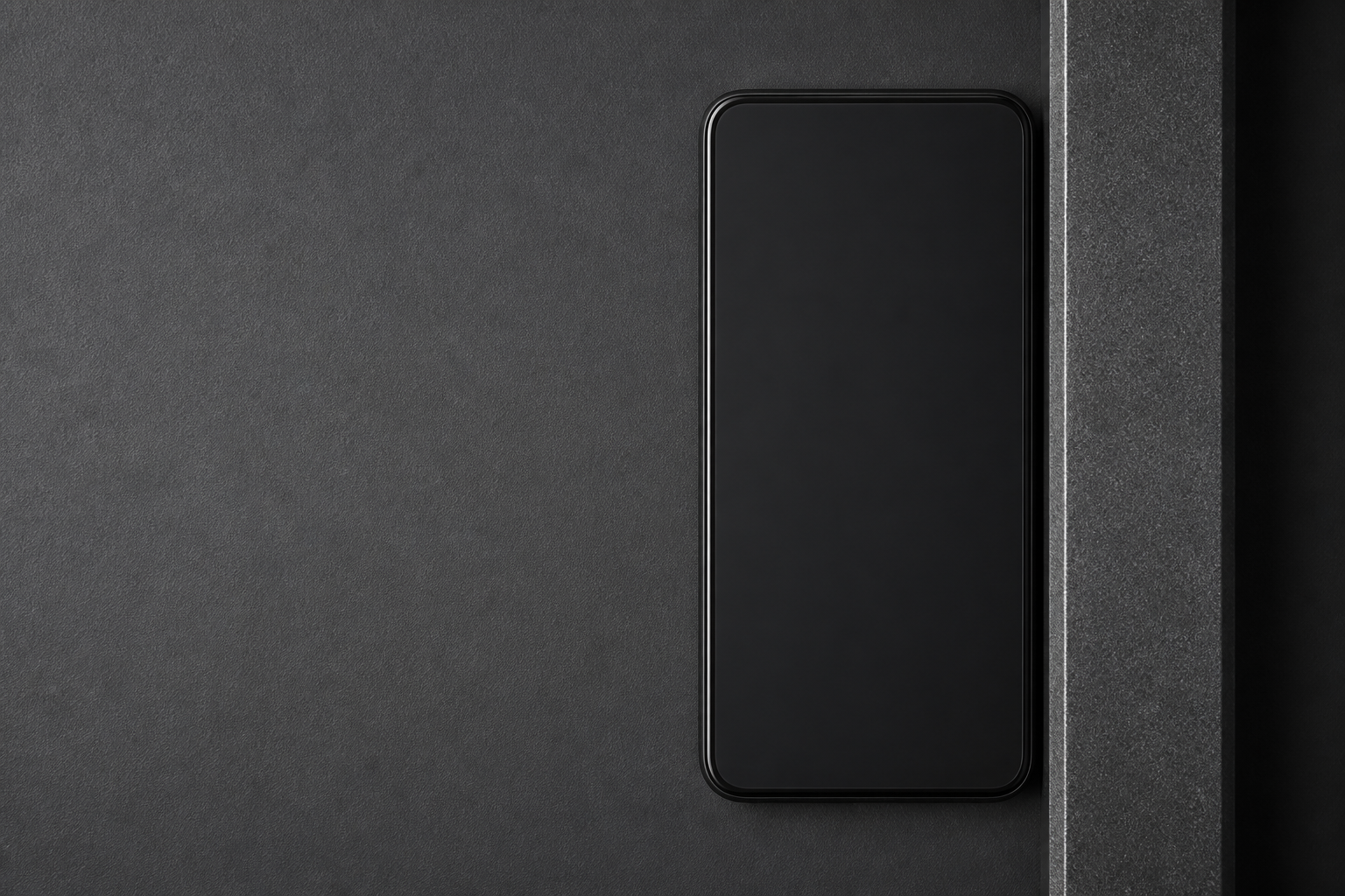 A dark phone precisely docked beside a machined vertical datum on a graphite surface.